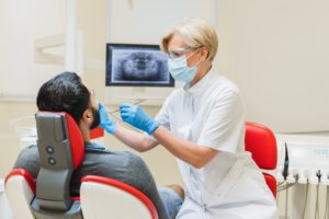 Stomatologist operating patient`s mouth cavity while checking x-ray photo of jaws in dental clinic