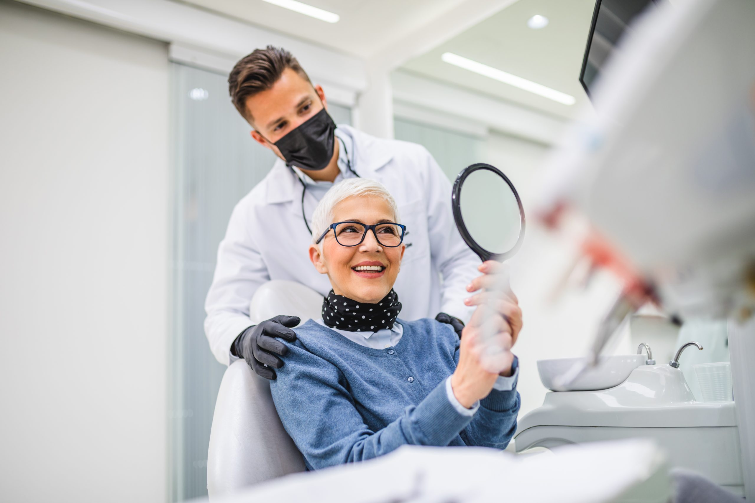 Beautiful senior woman having dental treatment at dentist's office. Dentist is wearing protective face mask due to coronavirus pandemic..